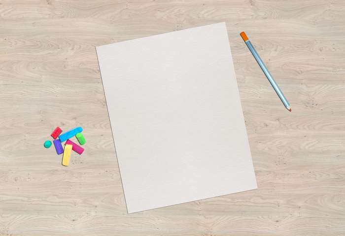 Blank paper with colored chalks and a pencil on a wooden surface