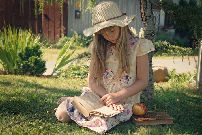 Girl in a hat reading a book outdoors