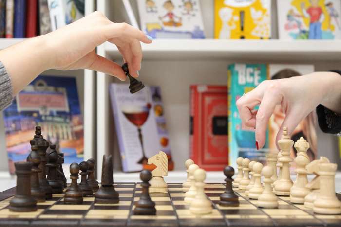 Hands playing chess with books in background