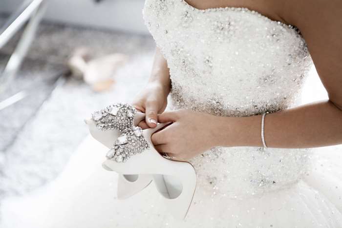 Bride holding embellished high heels, wearing a sparkling wedding dress