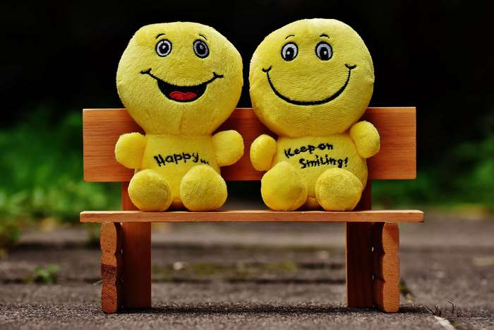 Two smiley stuffed toys on a wooden bench