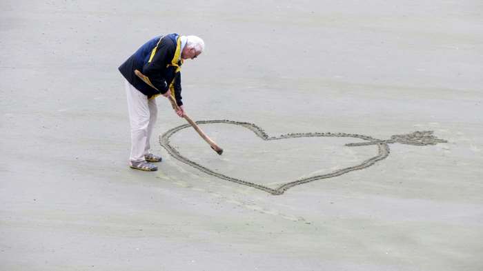 Elderly man drawing a heart in the sand on the beach