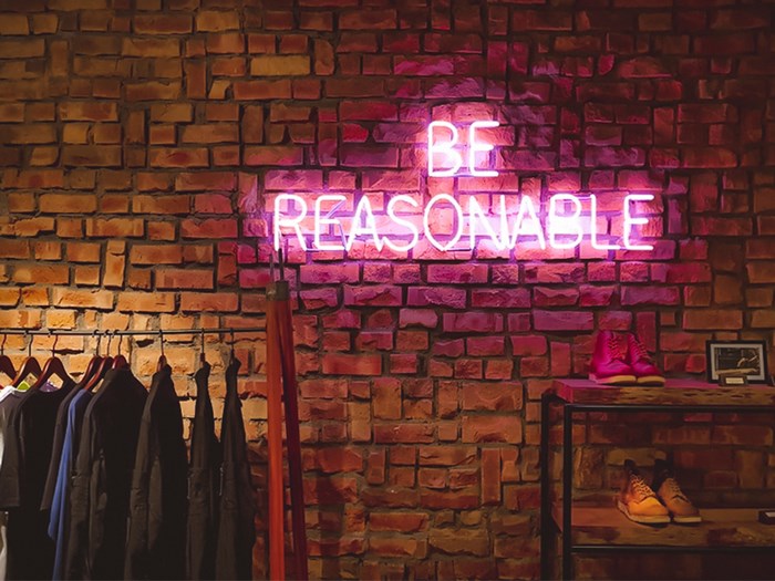 Neon sign "BE REASONABLE" on a brick wall