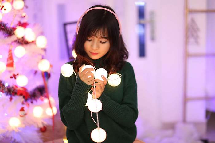 Young woman with headphones holding Christmas lights