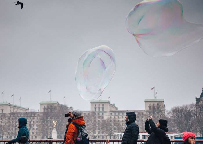 People watching giant bubbles float by buildings