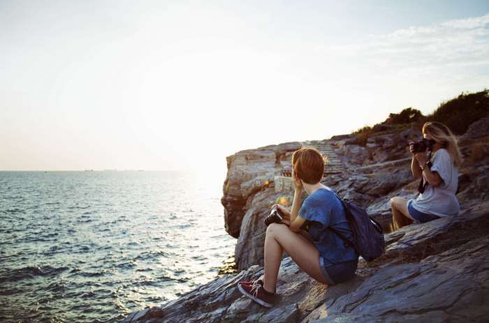 Two women with cameras on a rocky cliff by the ocean