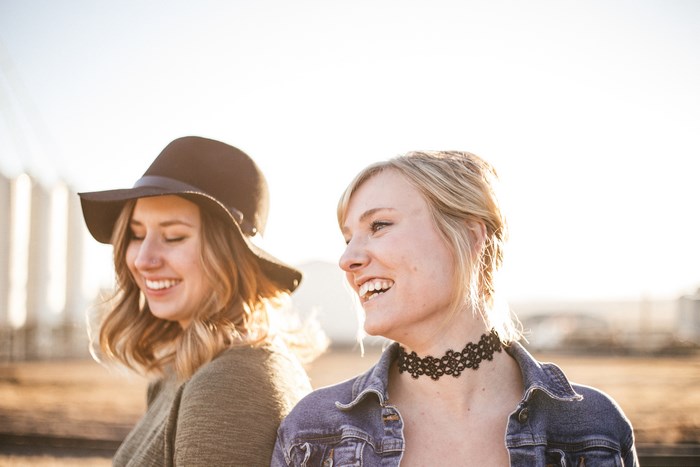 Two women laughing outdoors with a hat and choker