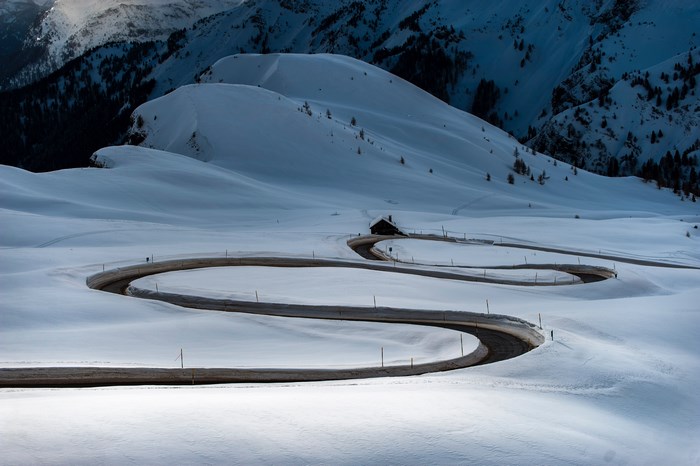 Winding road through snowy mountains with a small cabin