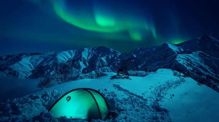 Tent under Aurora Borealis in snowy mountains