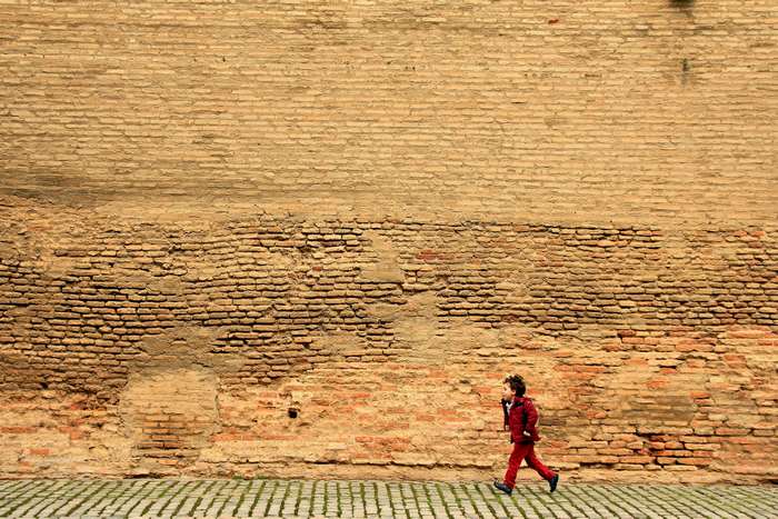 Child in red running along a brick wall