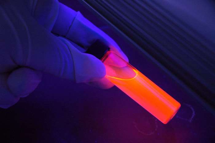 Gloved hand holding glowing orange liquid in test tube under UV light