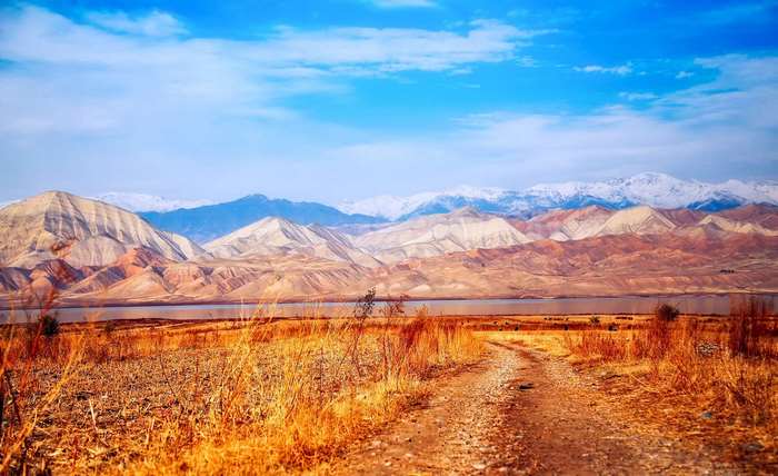 Dirt road leading to mountains and a lake in Kyrgyzstan