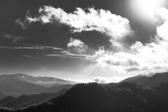 Black and white mountain landscape with sunlit clouds