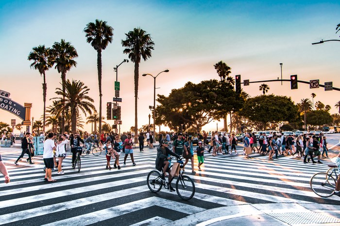 People and cyclists at a busy Santa Monica street crossing at sunset