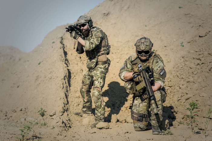 Two soldiers in camouflage uniforms with weapons in a desert environment