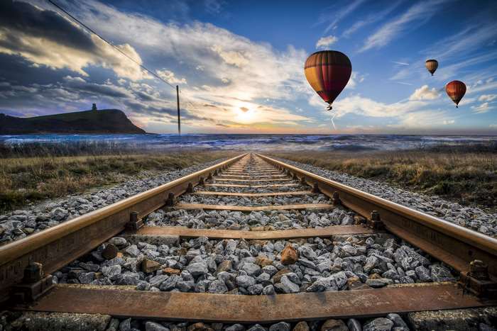 Railroad tracks leading to the ocean with hot air balloons at sunset