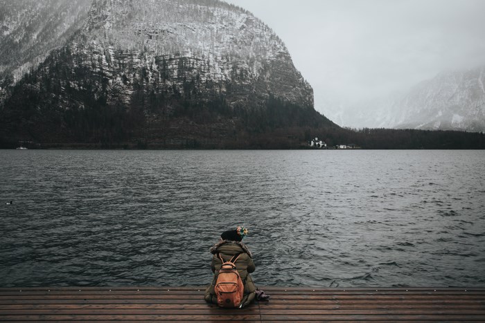 Person with backpack sitting on dock at Hallstatt lake in winter