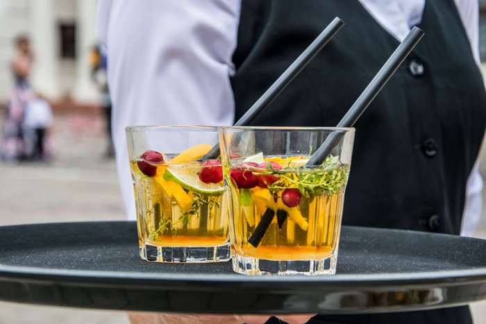 Two cocktails with fruit and straws on a tray