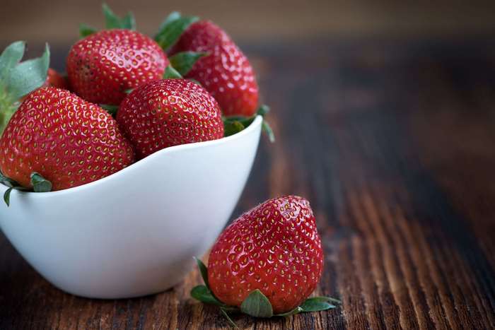 Strawberries in a white bowl on a wooden table