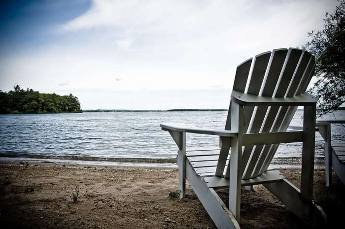 Adirondack chairs on a sandy beach by a lake