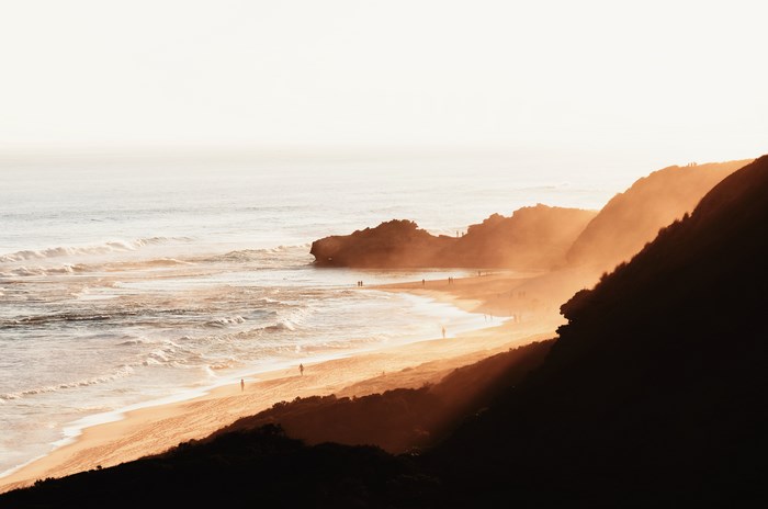 People walk along a beach at sunset with waves crashing
