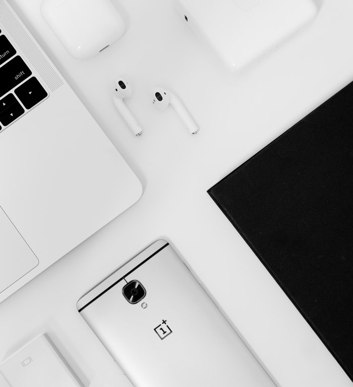 White laptop, phone, and earbuds on a white surface