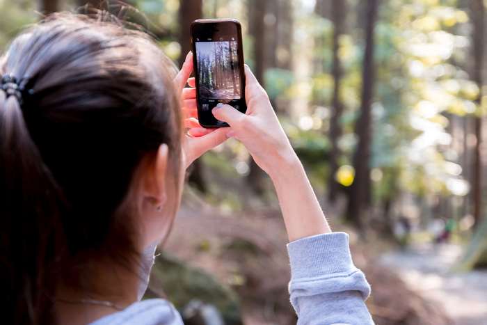 Woman taking a picture of a forest with her smartphone