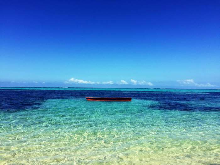 A lone red boat floats on clear turquoise ocean water