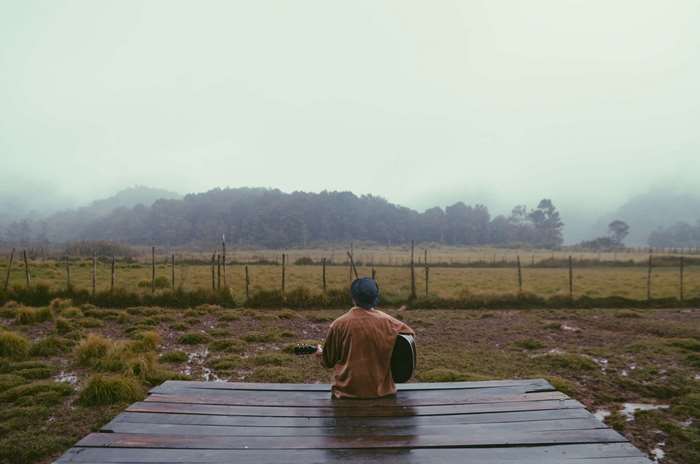 Man playing guitar on wooden platform in foggy landscape