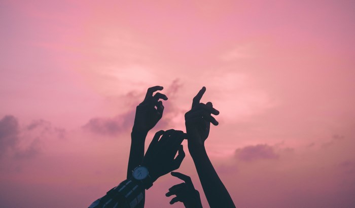 Silhouette of hands reaching towards a pink sky at sunset
