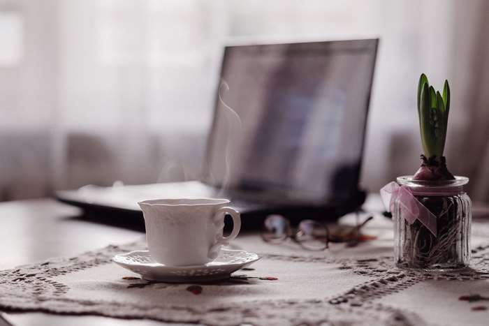 Steaming cup of coffee on a table with a laptop and plant