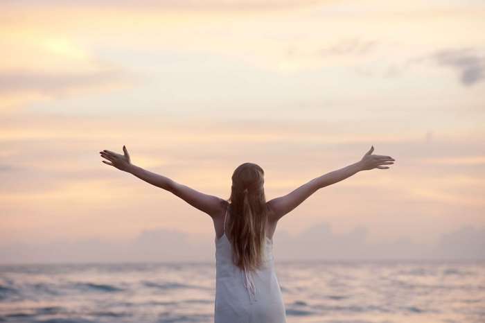 Woman with arms outstretched at the ocean during sunset
