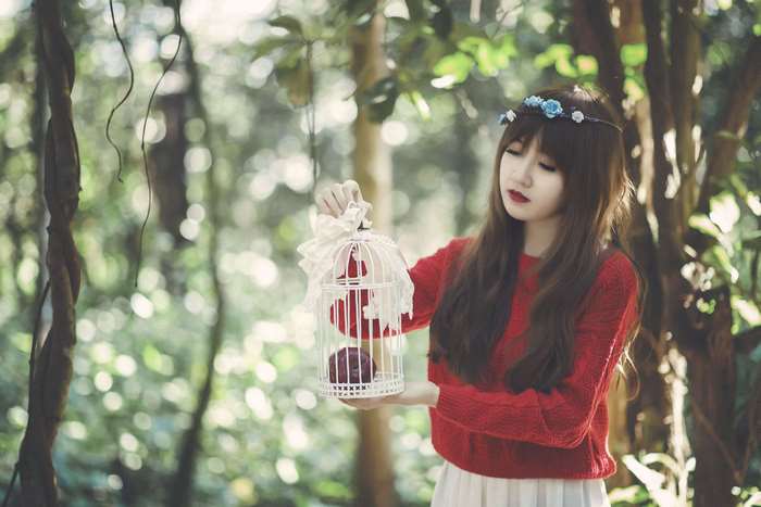 Young woman holding a decorative birdcage in a forest