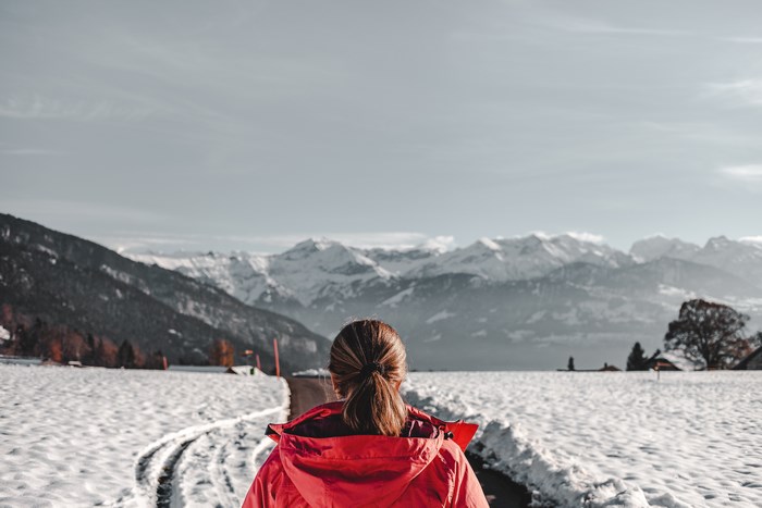 Woman in red jacket walking on snowy path towards mountains in Switzerland