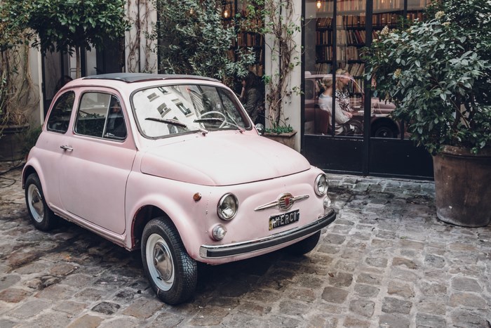 Pink vintage Fiat 500 parked on cobblestone street