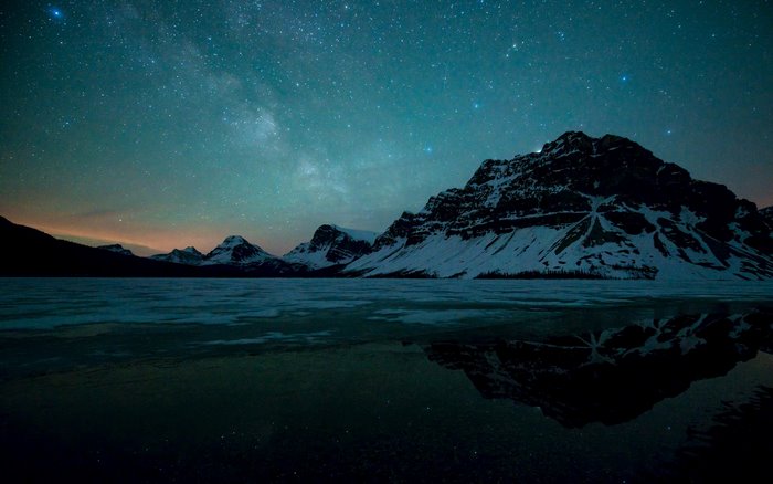 Snowy mountains under starry night sky with reflection