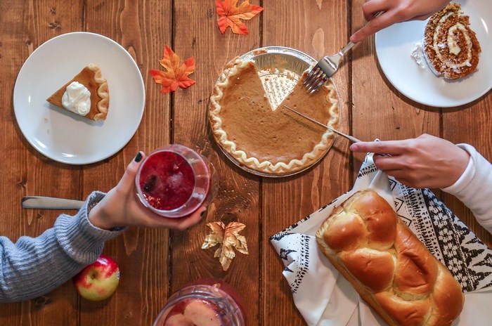 People slicing pumpkin pie and brioche bread on a wooden table