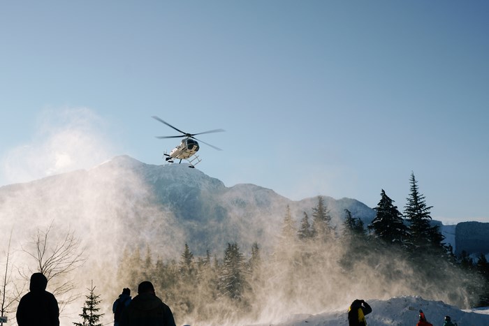 Helicopter landing on a snowy mountain with people watching