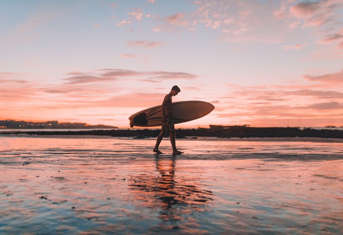 Man carrying surfboard on beach at sunset