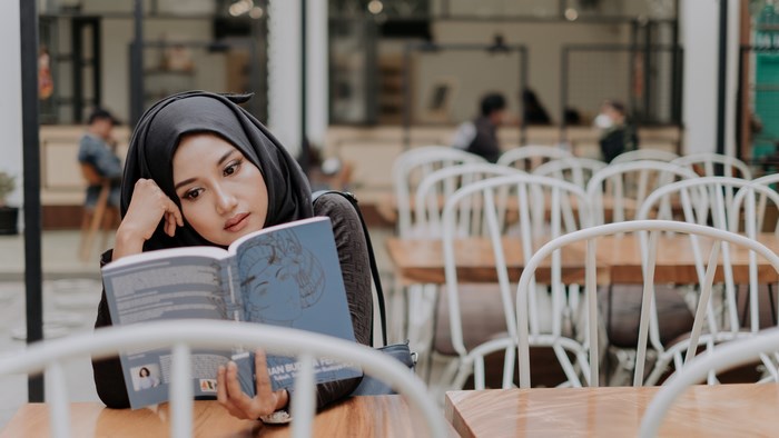 Woman in Hijab Reading a Book at a Cafe
