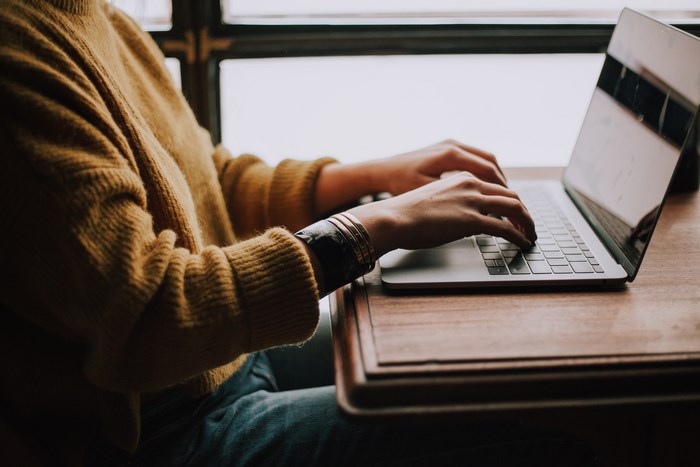 Person typing on a MacBook on a wooden desk