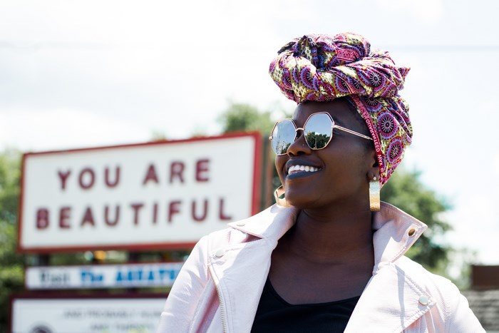 Woman wearing a turban and sunglasses in front of a sign