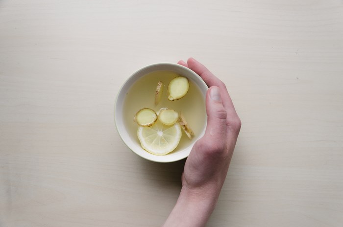 Hand holding a bowl of ginger tea with lemon