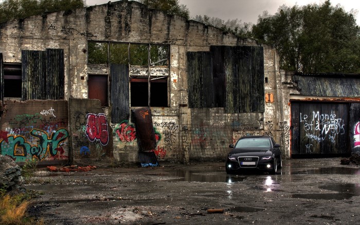 Black Audi parked in front of a graffiti-covered abandoned building