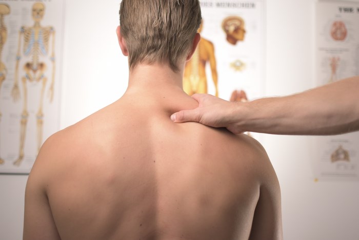 Man receiving shoulder massage with anatomical charts