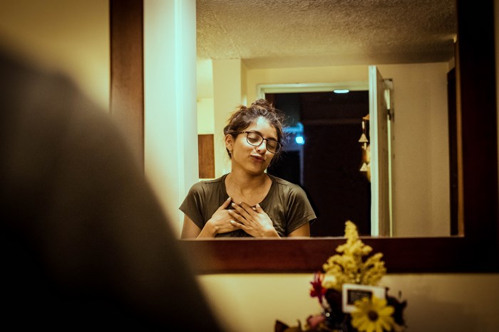 Woman with glasses touching her chest in a mirror