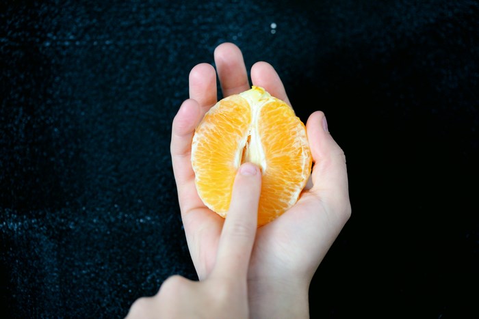 Person holding a peeled orange slice with finger