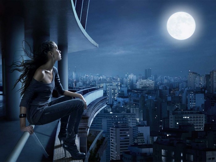 Woman on balcony overlooking city at night with moon