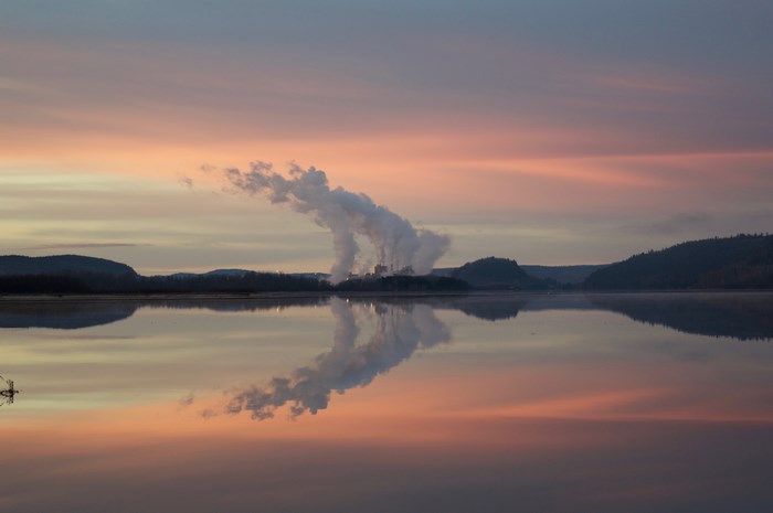 Factory smoke reflecting on a lake at dawn