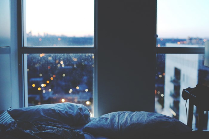 Bed with pillows by the window overlooking city lights at dusk
